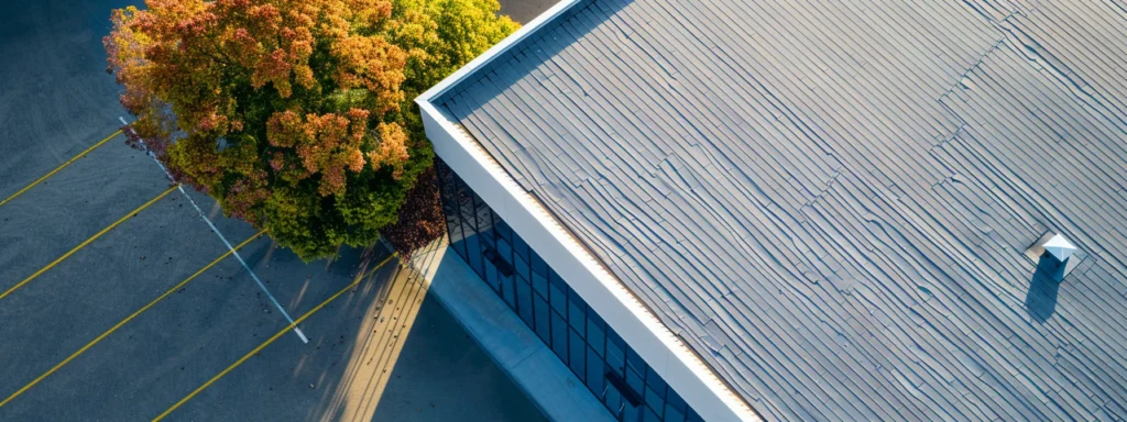 a captivating aerial view of a modern commercial building with a gleaming asphalt shingle roof under a bright blue sky, highlighting the importance of selecting the ideal roofing system based on environmental factors and building specifications.